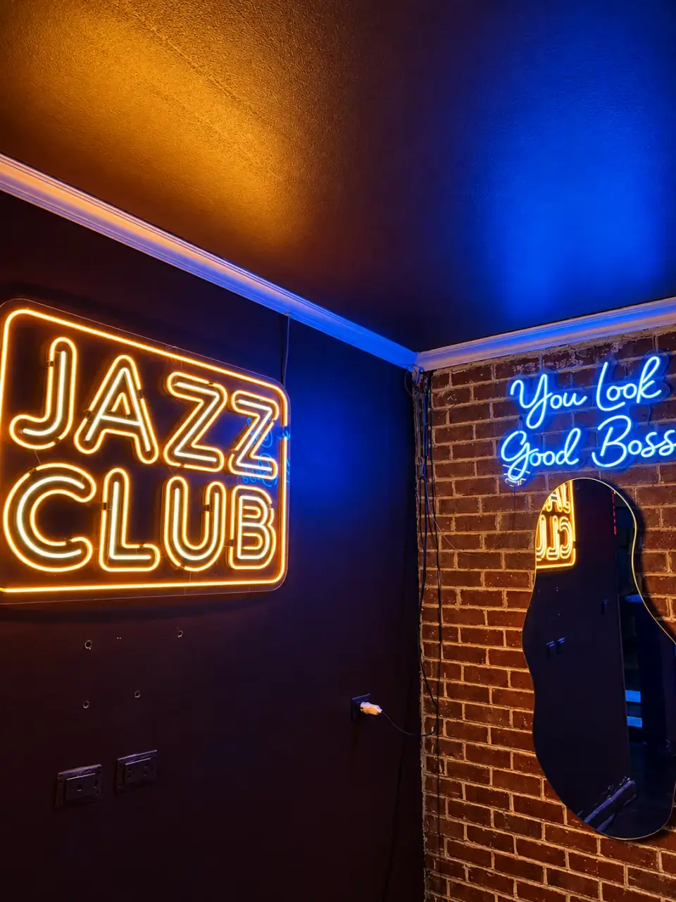 لافتة JAZZ CLUB النيون بجانب لافتة You Look Good Boss الزرقاء على جدار من الطوب